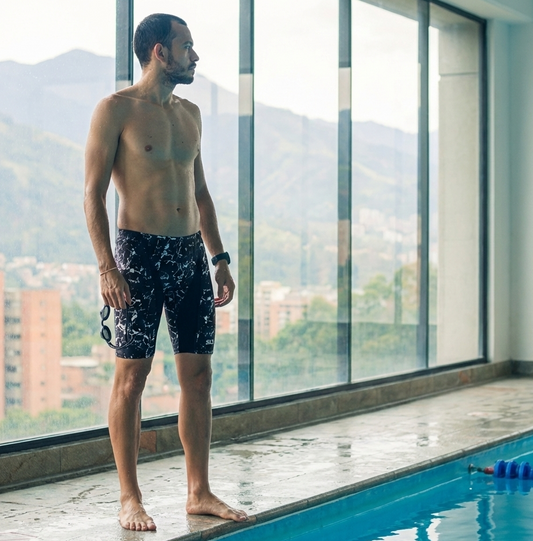 Man standing by a pool with mountains visible through large windows