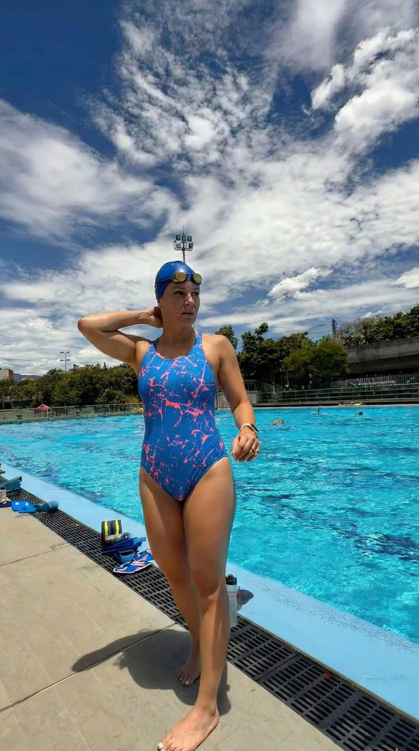 Person in a colorful swimsuit standing by a pool with a blue sky and clouds in the background