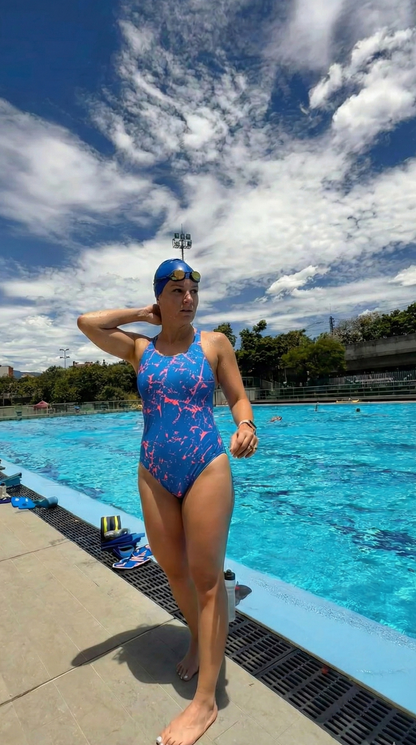 Person in a colorful swimsuit standing by a pool with a blue sky and clouds in the background